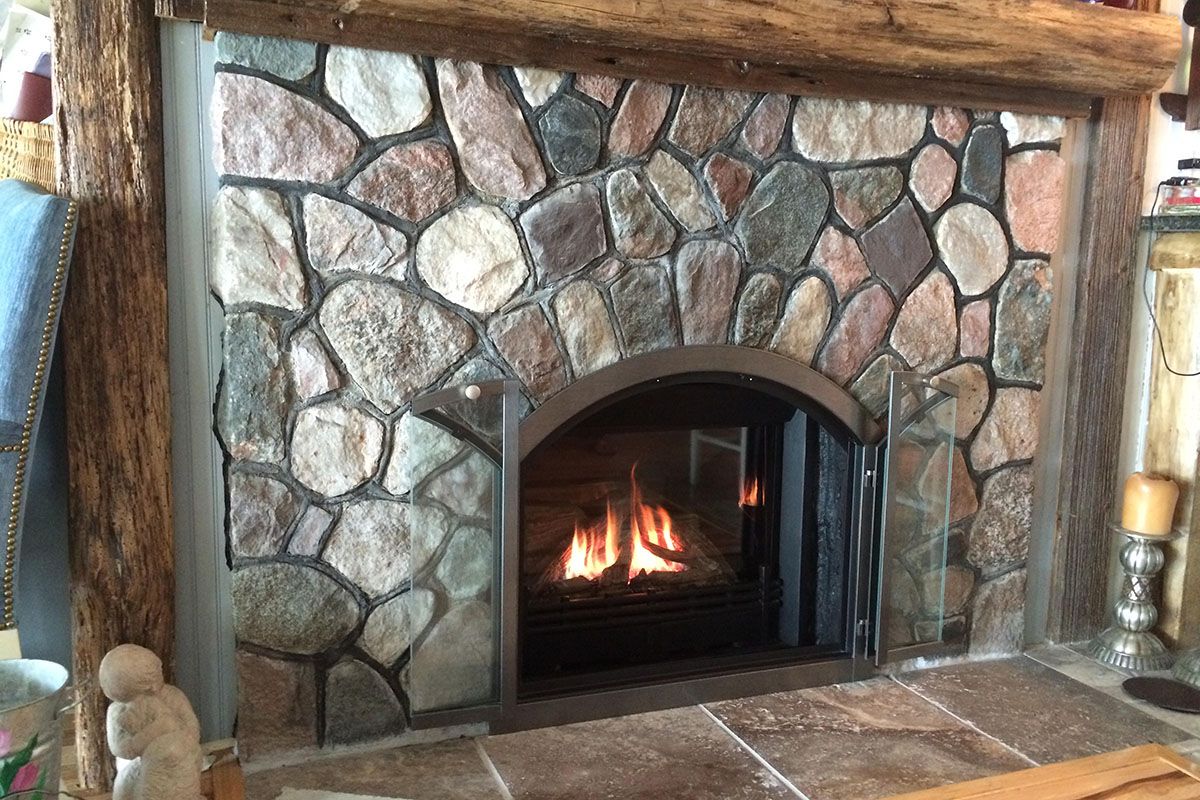 Arched Stoll doors fitted to a fieldstone fireplace with a fire burning