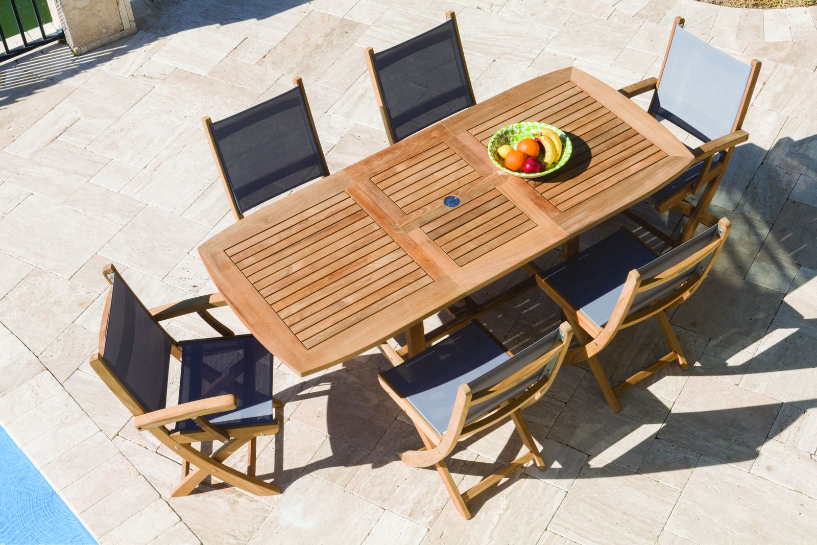 An overhead view of a teak rectangular dining table with folding sling chairs on a stone patio