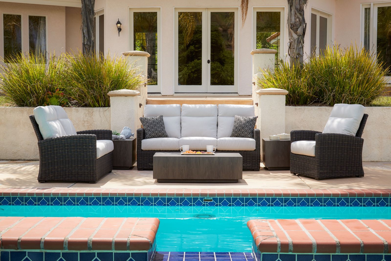 The Patio Renaissance Eureka resin-wicker sofa set with pale blue cushions beside a pool