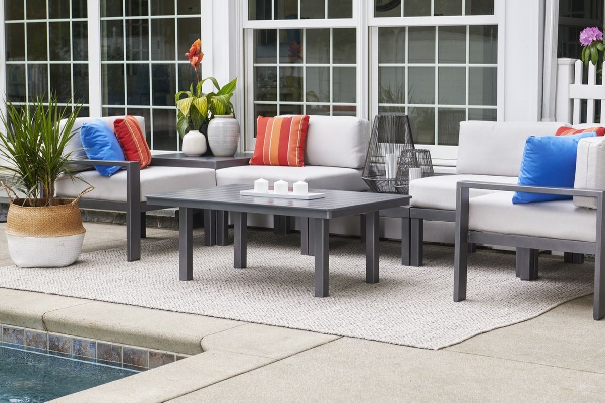 An aluminum-frame deep-seating sectional with white cushions and bright pillows on a stone patio