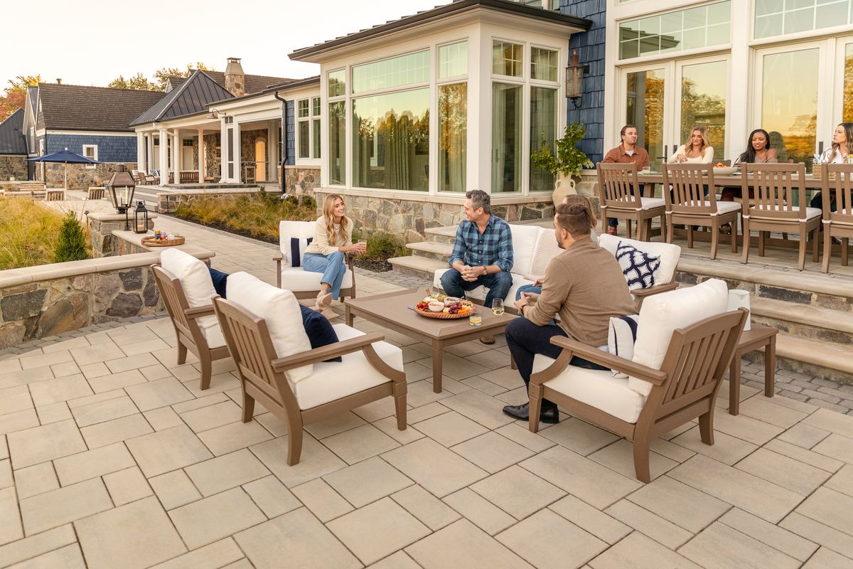 A poly-lumber dining and lounge set on a flagstone patio outside a stone house